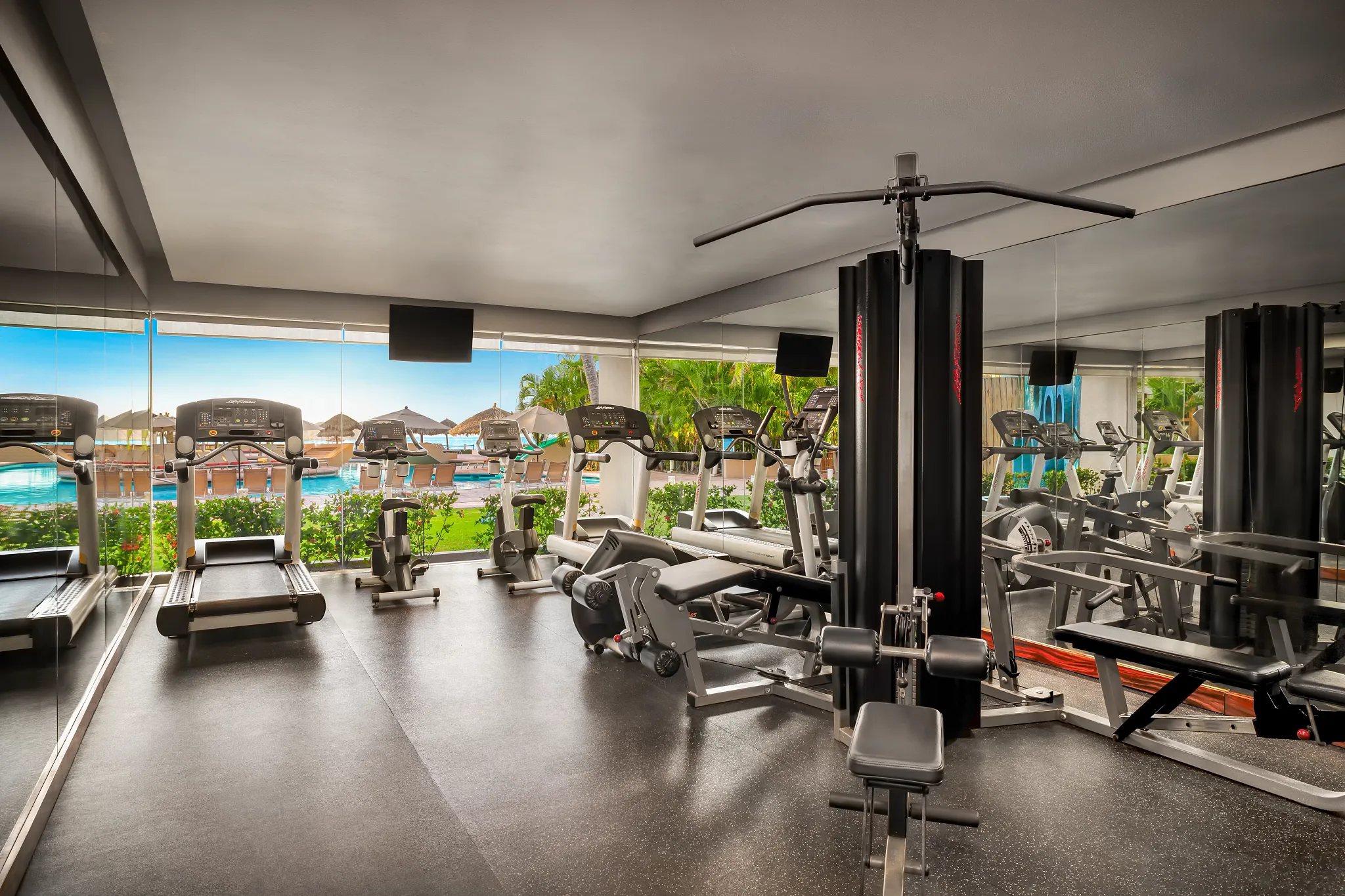 Modern fitness center with cardio and weight equipment overlooking the pool at Sunscape Dorado Pacifico Ixtapa.